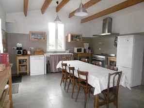 Une cuisine avec des poutres en bois, une table à manger avec des chaises, un réfrigérateur, un four à micro-ondes, une cuisinière et une fenêtre avec des rideaux.