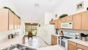 A modern kitchen with wooden cabinets, a microwave, stove, and a sink. - Entire Villa with Pool and great Privacy near Disney (Kissimmee)