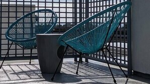 Terraza en la azotea con dos sillas verdes y una mesa de hormigón, delimitada por una valla de metal negro.