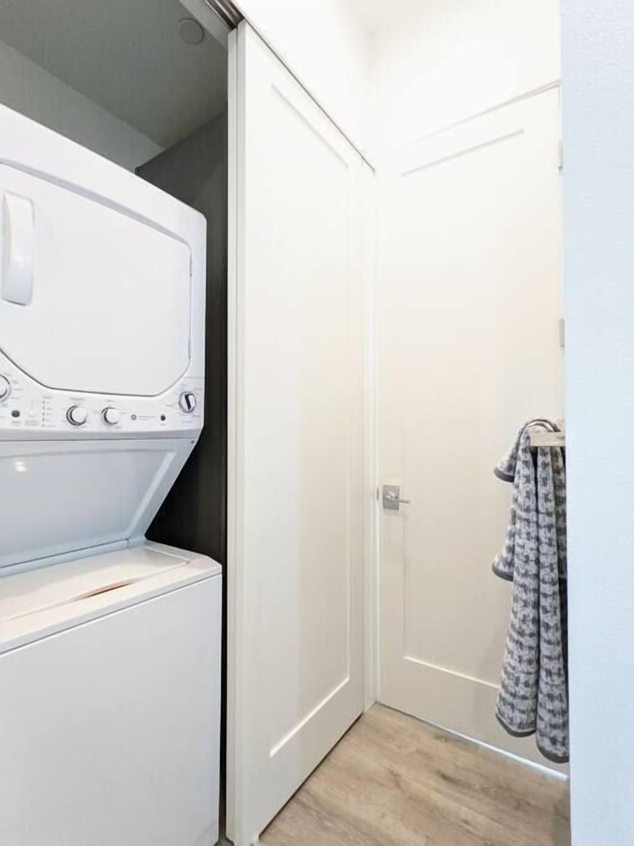 A laundry room with a white washing machine and dryer, a closed door, and a towel rack with patterned towels.
