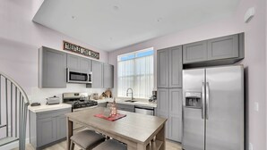 Una cocina moderna con armarios grises, un refrigerador de acero inoxidable, un horno empotrado y una ventana con cortinas translúcidas.