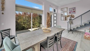 A modern dining area with a large wooden table, chairs, and a view of the outdoors.