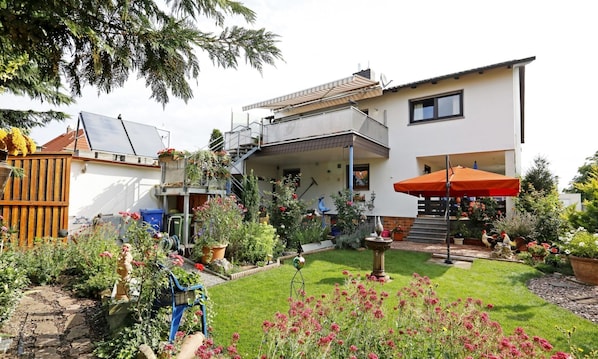 A two-story house with a covered patio, a garden with various plants and flowers, and a small birdbath.