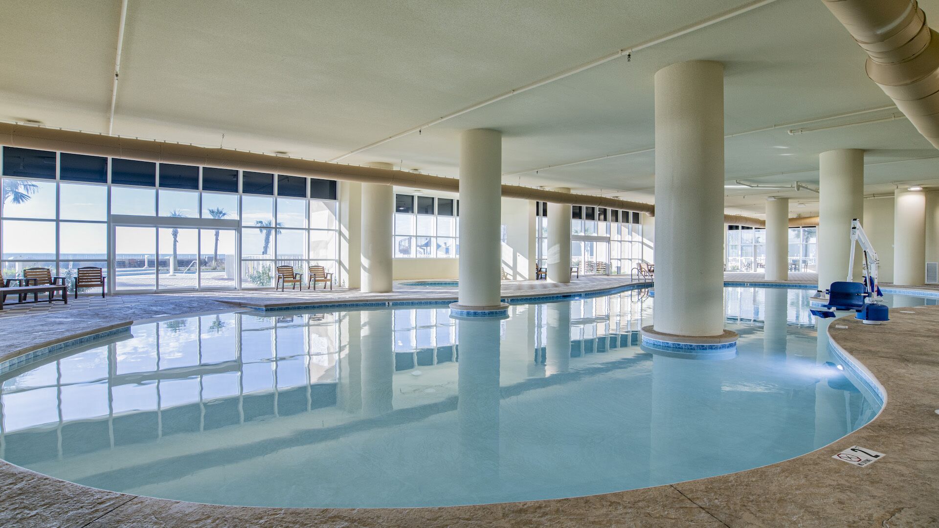 Une piscine intérieure avec des parois en verre transparent, de grandes colonnes et quelques chaises longues.