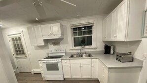 A kitchen with white cabinets, a stove, a sink, and a toaster. - Cozy Cottage in Snug Harbor, minutes to the beach (pet friendly) (South Kingstown)