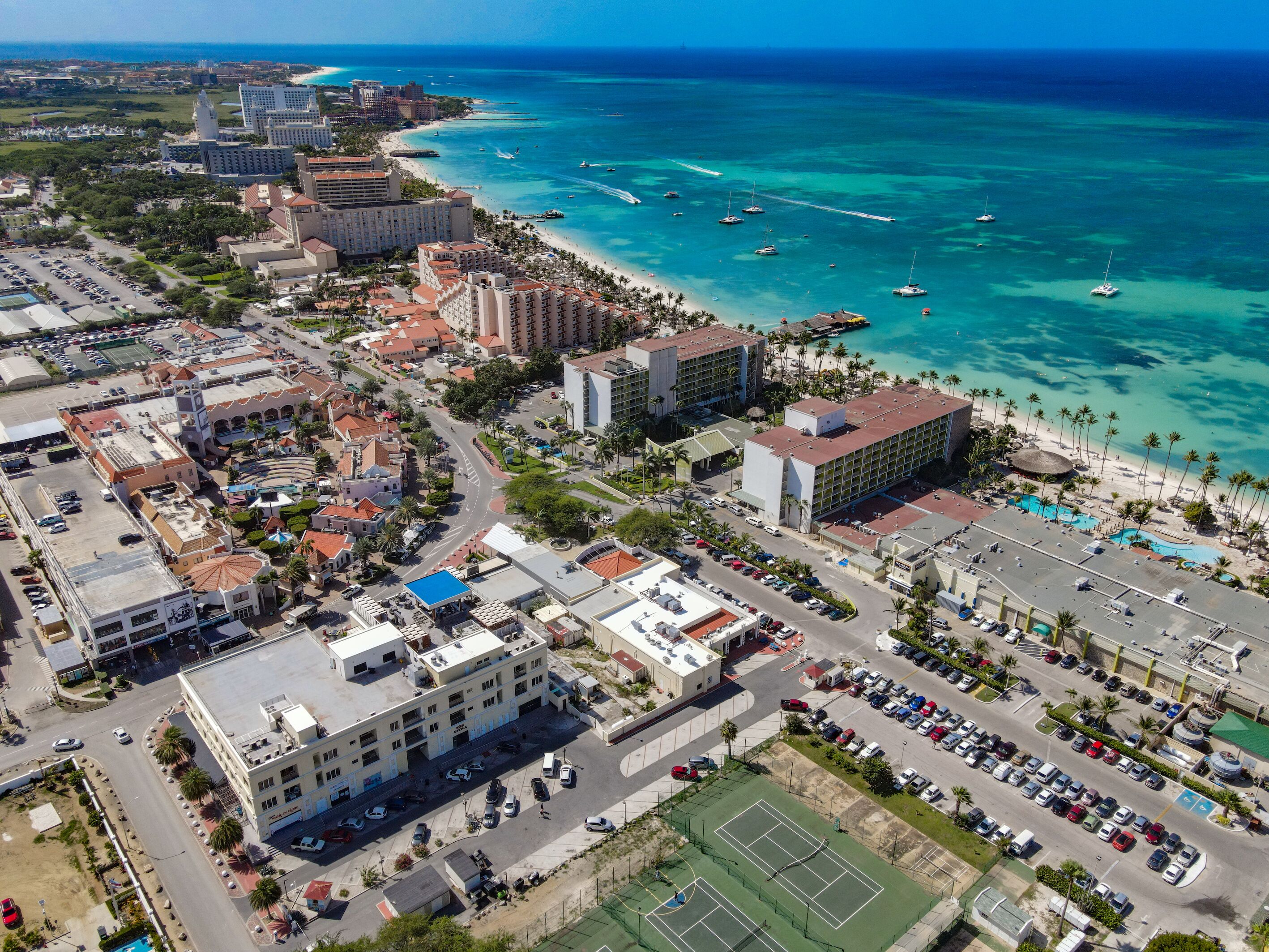 Vista aérea de una ciudad costera con playa, hoteles y una cancha de tenis.