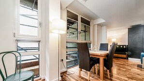 A modern dining area with a wooden table, two chairs, a floor lamp, and a view of a balcony with a railing.