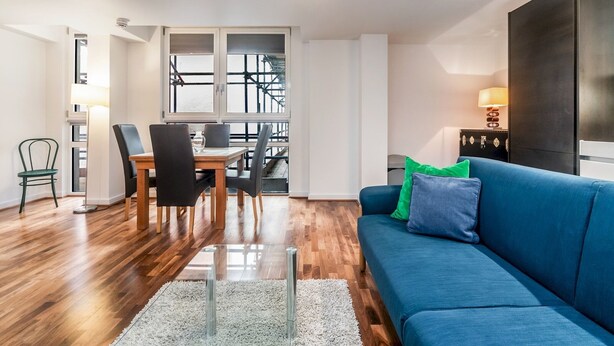 A modern living room with a blue sofa, a dining table with chairs, and a view of a bridge through large windows.