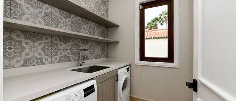 A compact laundry room with a Bosch washing machine, a sink, and patterned tile walls.