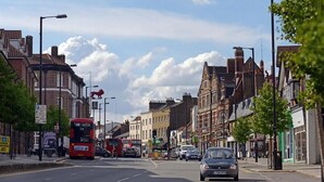 Une scène de rue avec des bâtiments traditionnels, un autobus à deux étages rouge et une voiture.