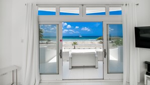 Una habitación con puerta de cristal que da a un balcón con vista a una playa y al océano.