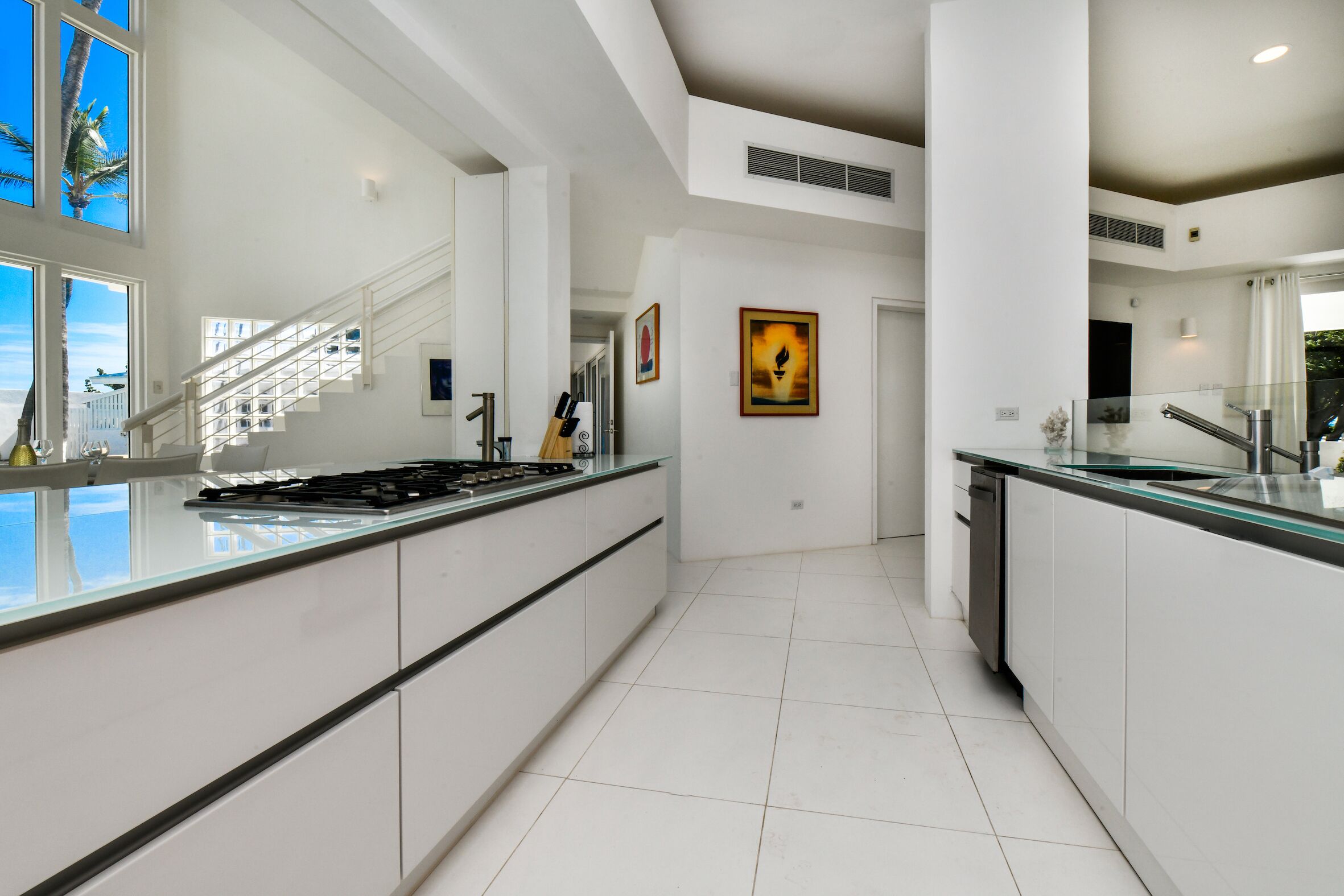 A modern kitchen with a large island, white cabinetry, and a view of the beach through large windows.