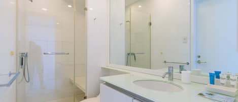 A modern bathroom with a glass shower enclosure, a white toilet, and a large mirror above a sink with toiletries.