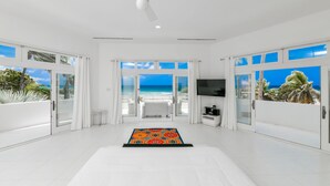 Una habitación amplia con una cama grande, ventilador de techo y vista a la playa a través de puertas de vidrio.