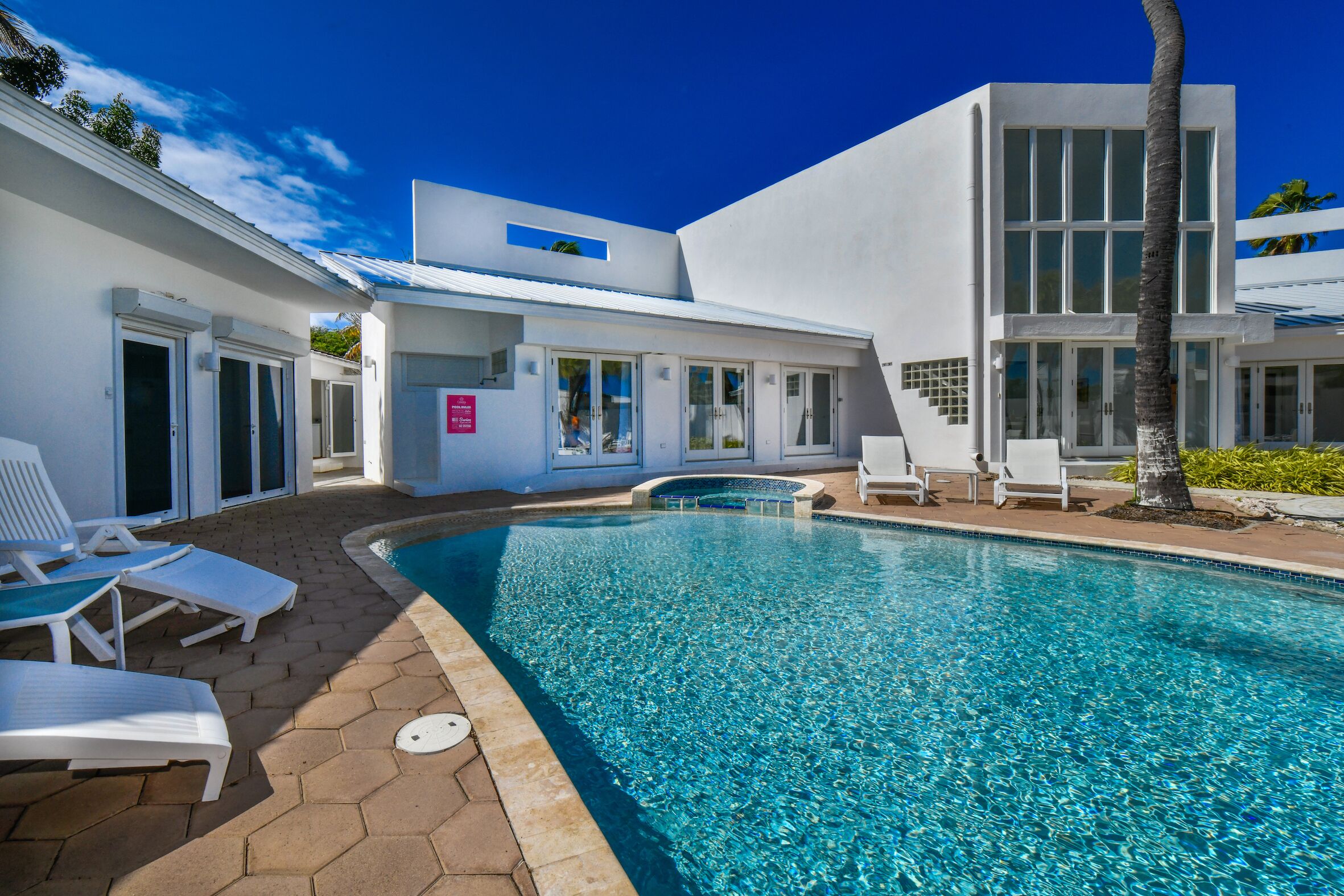 Un bâtiment moderne doté d’une piscine, d’une façade blanche et surplombé d’un ciel d’un bleu limpide.