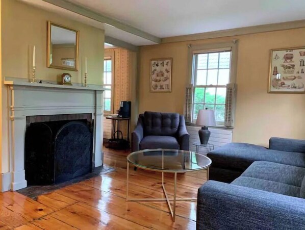 A living room with a fireplace, a sofa, a glass coffee table, and artwork on the walls.