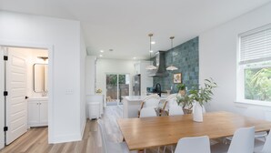 A modern kitchen with white cabinetry, a wooden dining table, and a view of the outdoors. - Brand new 4 bedroom with 2  master suites and pool, steps to the beach. (St. Augustine)