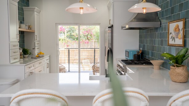 A modern kitchen with white cabinetry, a central island, pendant lighting, and a view to a backyard. - Brand new 4 bedroom with 2  master suites and pool, steps to the beach. (St. Augustine)