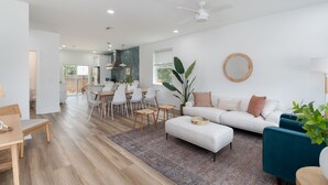 A modern living room with a white sofa, blue armchairs, and a dining area with white chairs and a table. - Brand new 4 bedroom with 2  master suites and pool, steps to the beach. (St. Augustine)