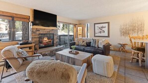 A living room with a stone fireplace, a black leather sofa, and a dining area with wooden furniture.