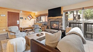 A cozy living room with a fireplace, wooden walls, and a large TV.