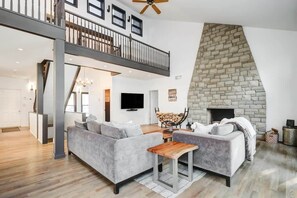 A spacious living area with a high ceiling, a stone fireplace, and a balcony. - Waterfront open concept dream cottage with hot tub (Portland)