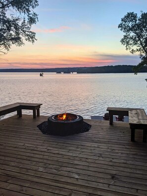 A wooden deck with a fire pit and benches overlooking a calm body of water at sunset. - Waterfront open concept dream cottage with hot tub (Portland)