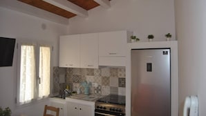 Eine Küche mit weißen Schränken, einem Edelstahl-Kühlschrank, einem Herd und einem Fenster mit Vorhängen.