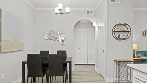 Un comedor con una mesa y sillas, una araña, un espejo en la pared y una puerta que da a otra habitación.