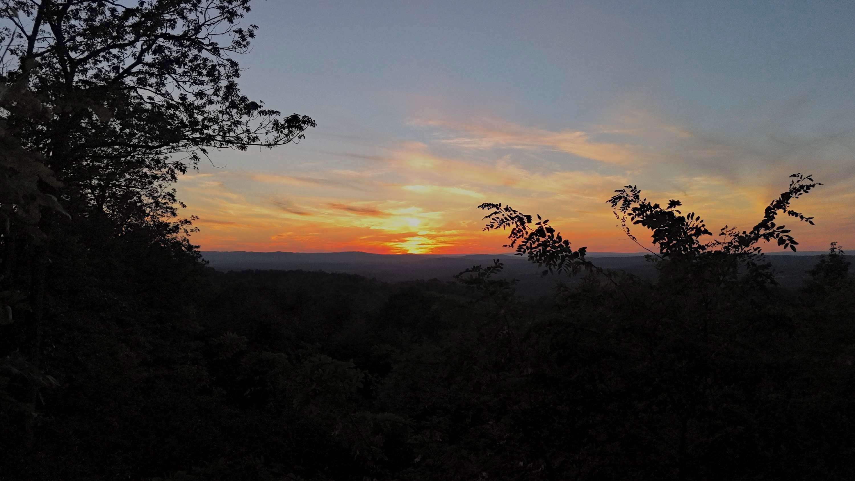 A sunset over a mountainous landscape with trees in the foreground.