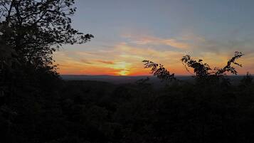 A sunset over a mountainous landscape with trees in the foreground.
