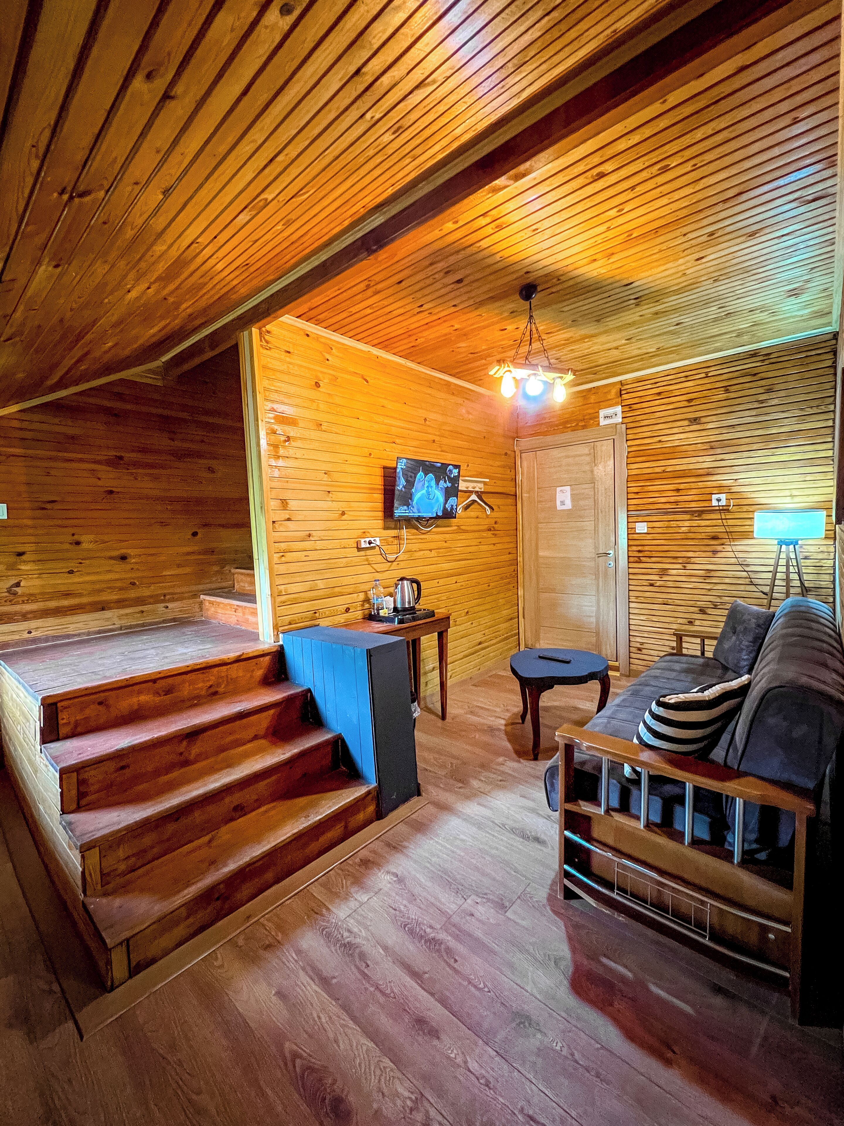 Ein Holzinterieur mit Treppe, einer Couch, einem Tisch und einem an der Wand montierten Fernseher.