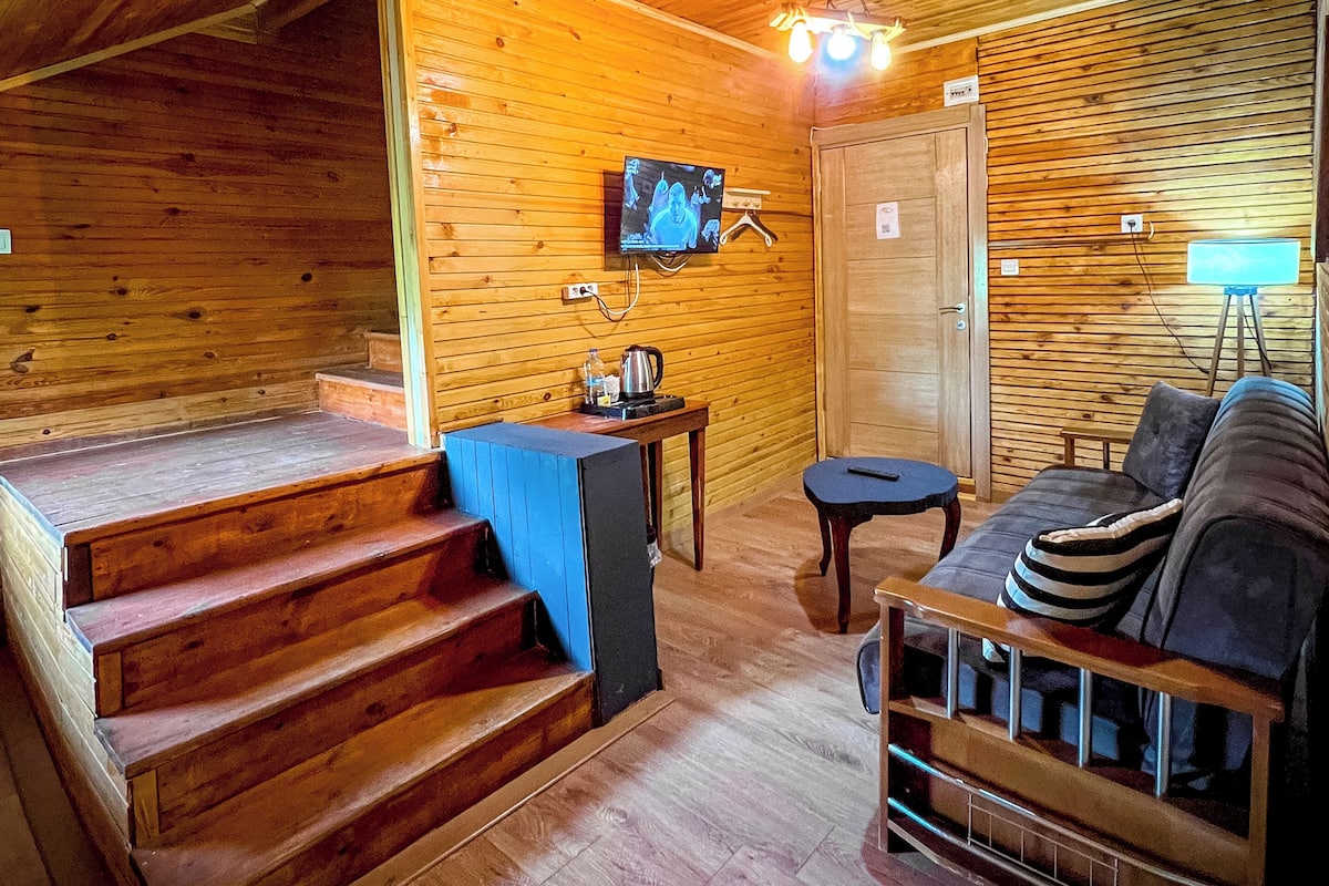 Ein Holzinterieur mit Treppe, einer Couch, einem Tisch und einem an der Wand montierten Fernseher.