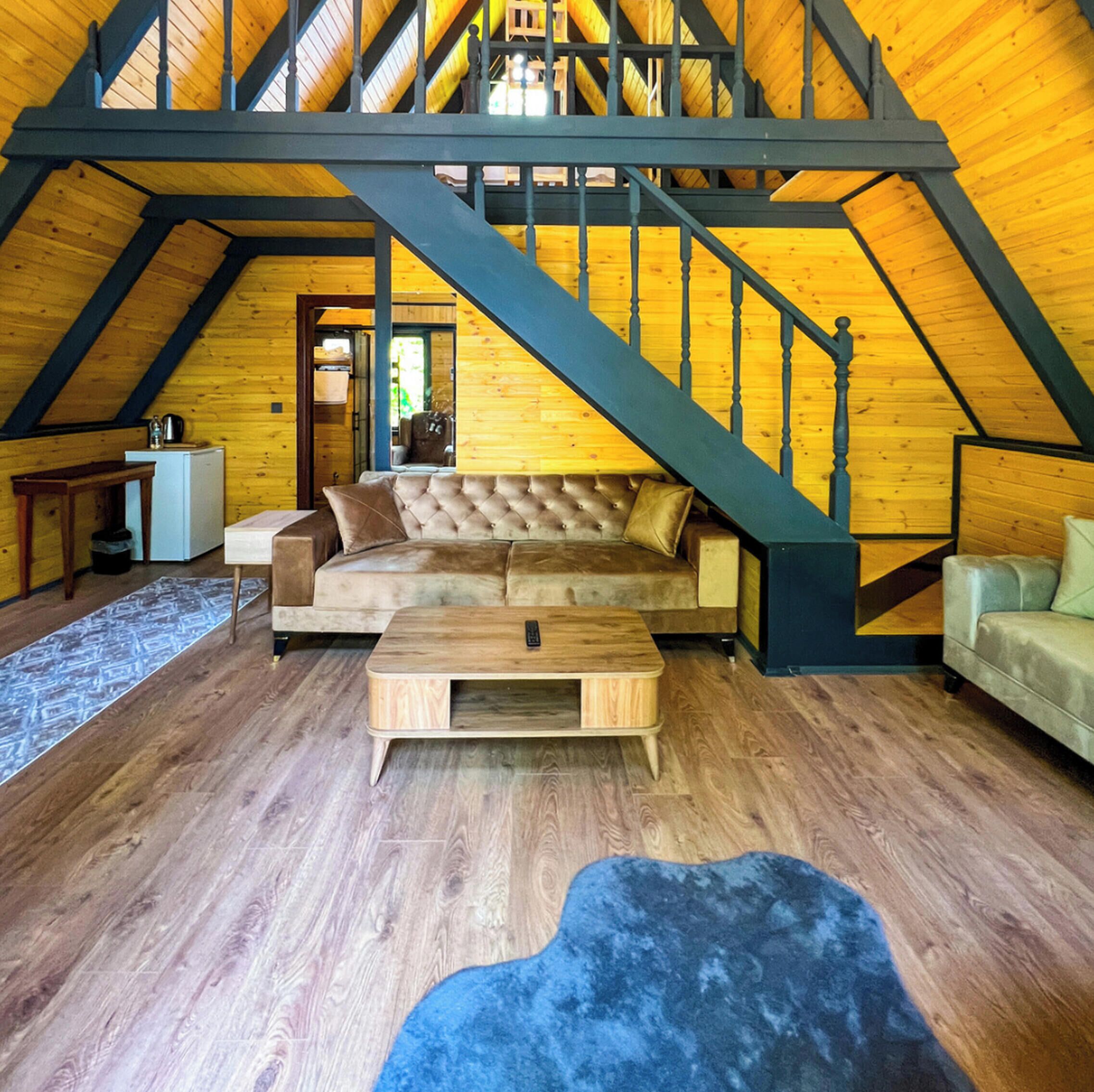 Ein Loft-Zimmer mit einer Holztreppe, einem gesteppten Sofa, einem Couchtisch und einem blauen Teppich.