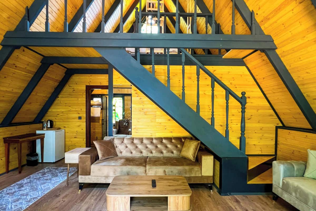 Ein Loft-Zimmer mit einer Holztreppe, einem gesteppten Sofa, einem Couchtisch und einem blauen Teppich.