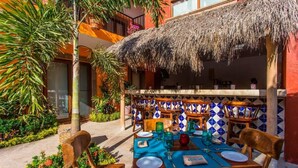 An outdoor dining area with a thatched roof, wooden tables, and chairs, surrounded by a garden with tropical plants. - Unique 2BR Suite at the Best Location in Sayulita (Sayulita)