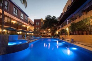 Zwembad met een jacuzzi, omringd door gebouwen met balkons en buitenverlichting.