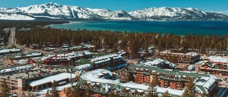 A resort area with multiple buildings, a parking lot, and a view of snow-capped mountains and a lake.