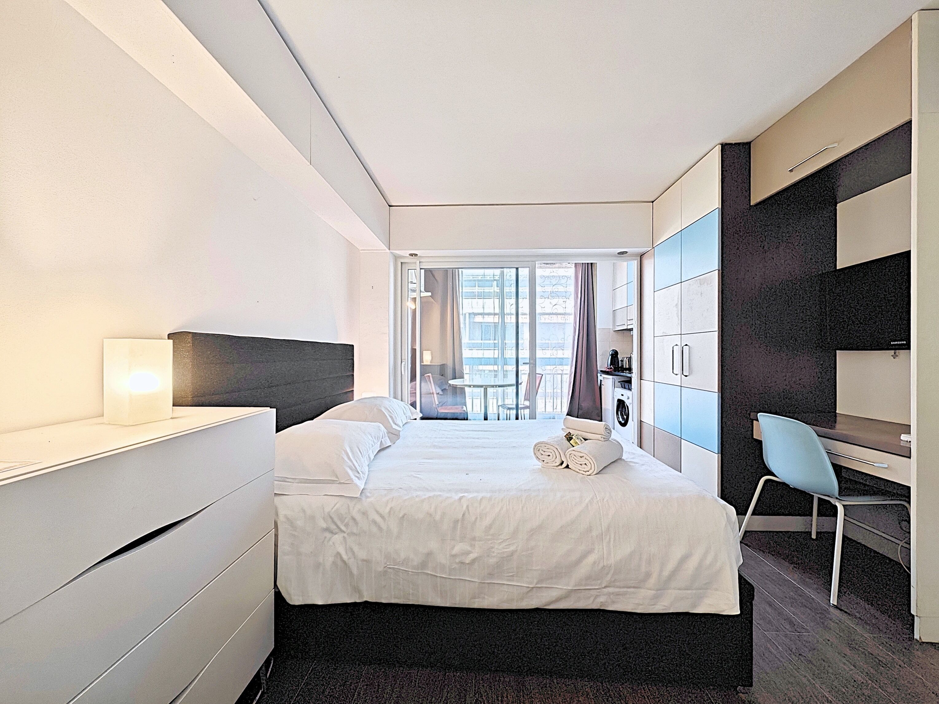 A modern hotel room with a large bed, a desk, and a view of the city through the window.