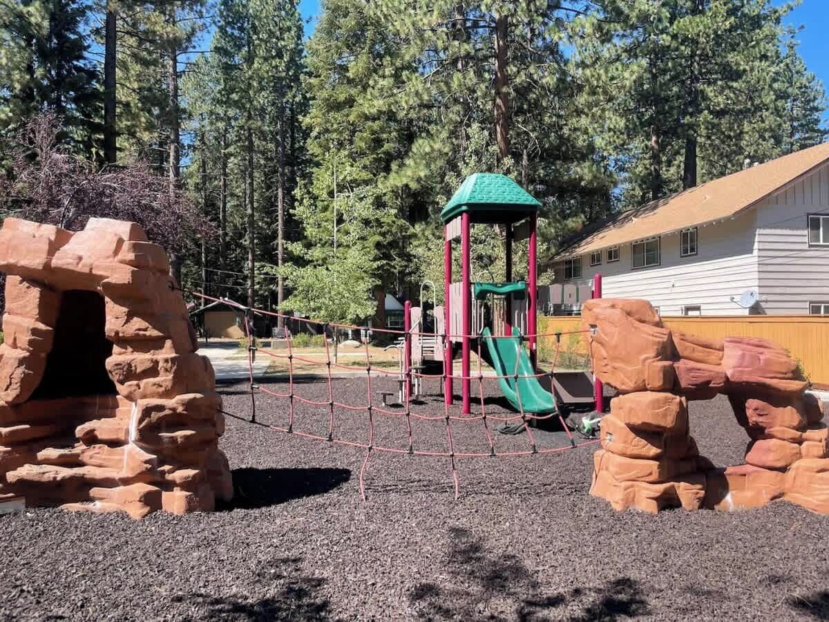 Un terrain de jeux avec des structures d’escalade et un toboggan, entouré d’arbres et bordé d’un bâtiment.