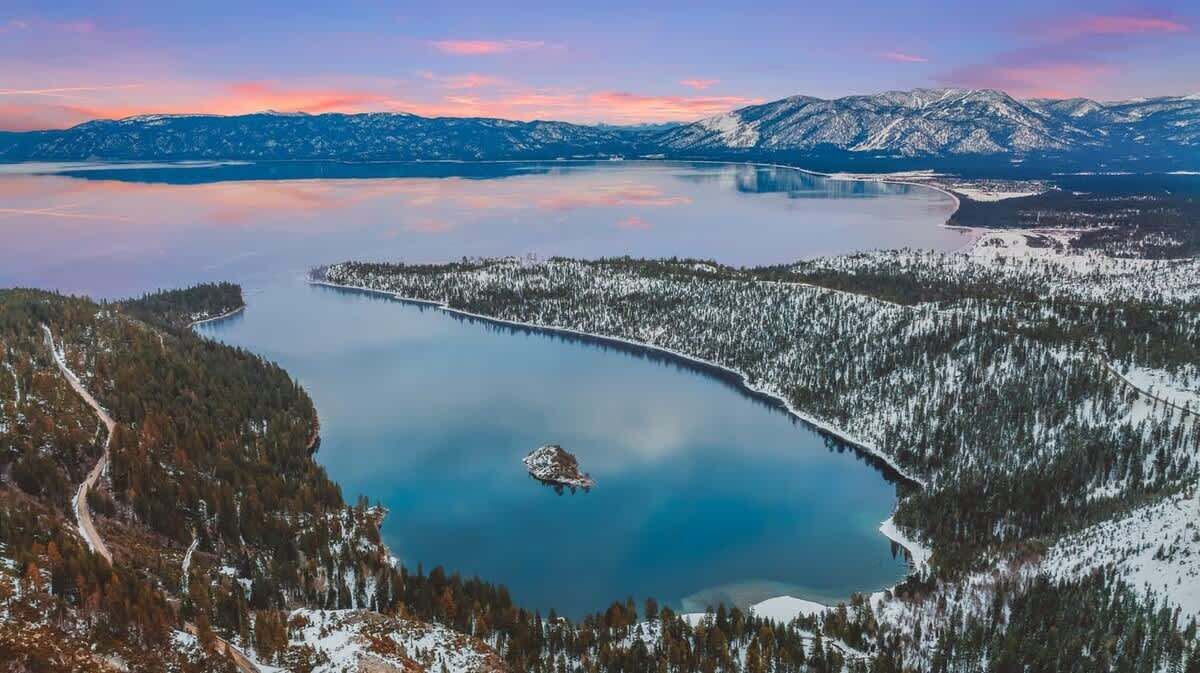 A panoramic view of a lake surrounded by snow-covered forests and mountains.