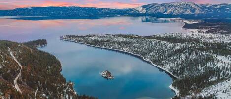 A panoramic view of a lake surrounded by snow-covered forests and mountains.