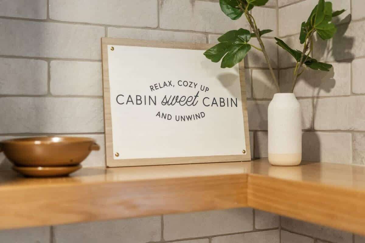 A framed sign with text on a wooden shelf, a white vase, and a brown bowl.