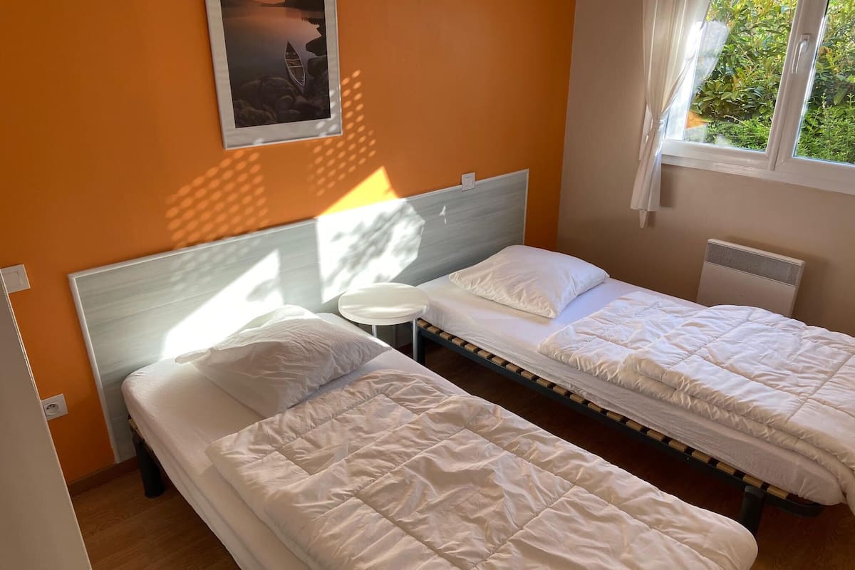 Una habitación con dos camas individuales, una mesita redonda, un cuadro colgado en la pared y una ventana con vistas a zonas verdes.