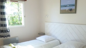 Une chambre d’hôtel avec deux lits, une fenêtre avec des rideaux, un tableau au mur et un sol carrelé.