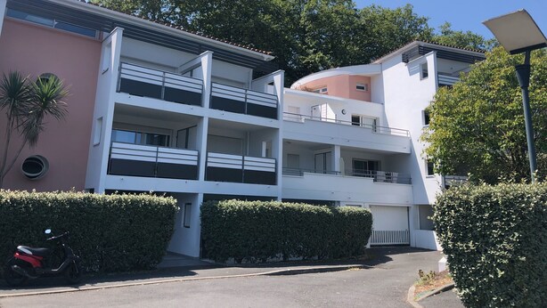 Een meerlaags woongebouw met balkons, een parkeerplaats en een scooter ervoor.