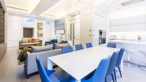Ein modernes Wohnzimmer mit Essbereich, ausgestattet mit einem weißen Marmortisch und blauen Stühlen.