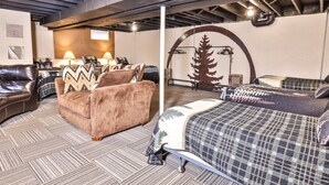 Camera d'albergo con un letto, un divano e una poltrona. Si nota una decorazione a forma di albero in legno sulla parete e una lampada sul tavolo.