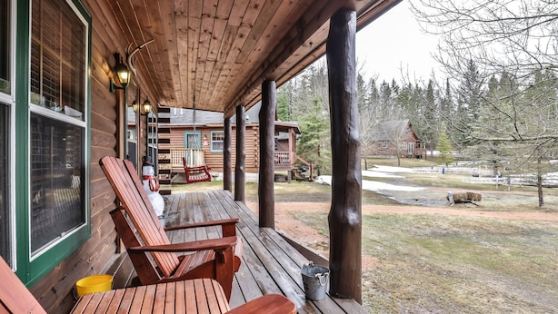 Une véranda en bois avec deux chaises en bois et un banc, une balançoire suspendue et une décoration représentant un bonhomme de neige.