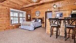 Une chambre aménagée dans un chalet en rondins, comprenant un lit, deux chaises, une table et un coin cuisine.